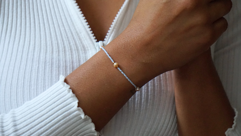 Zartes DIY-Armband in Hellblau mit goldfarbenen Details und Süßwasserperlen, getragen zu einem weißen, gerippten Oberteil mit Reißverschluss. Das Armband aus dem Schmuckset von ever so tiny verbindet minimalistische Eleganz mit nachhaltigem Design.