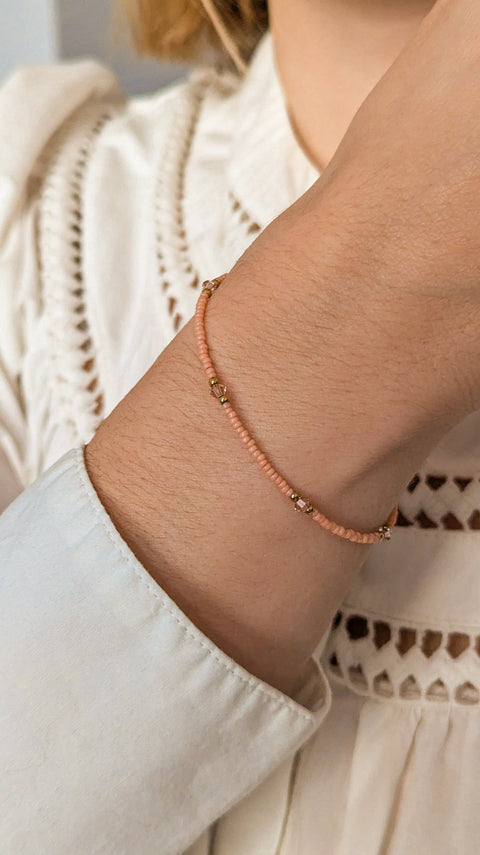 Zartes DIY-Armband in Apricot mit goldfarbenen Details und Swarovski-Kristallen, elegant kombiniert mit einer weißen, bestickten Bluse. Das Schmuckstück aus dem ever so tiny DIY-Set steht für hochwertigen, nachhaltigen und individuell gestaltbaren Schmuck.