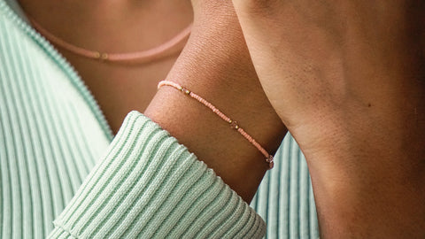 Zartes DIY-Armband in Peach mit goldfarbenen Details und Swarovski-Kristallen, kombiniert mit einer passenden Halskette im gleichen Design. Getragen zu einem mintgrünen, gerippten Oberteil, zeigt das Bild den eleganten und nachhaltigen Stil, den das Schmuckset von ever so tiny ermöglicht.