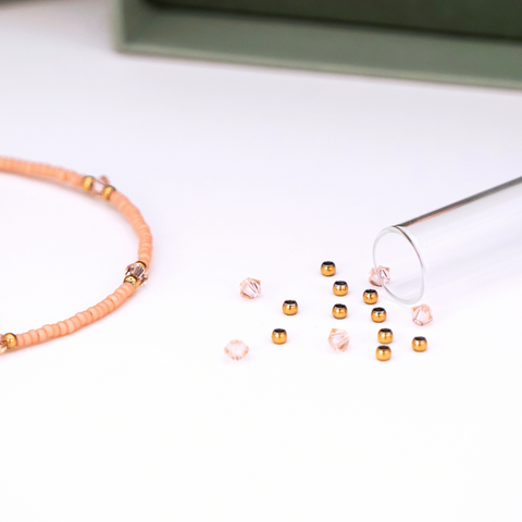 Close-Up auf DIY-Schmuckset von ever so tiny für ein Armband in zartem Apricot mit goldfarbenen Details und Swarovski-Kristallen. Das Set wird in einer eleganten, jadegrünen Box mit hochwertiger Goldprägung präsentiert und enthält alles, was für die Schmuckherstellung benötigt wird: Glasperlen, Verschluss, Werkzeug und eine Anleitung für einfaches Selbermachen. Im Vordergrund ist ein fertiges Beispielarmband zu sehen.