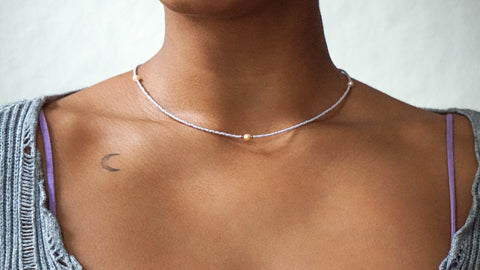 Zarte DIY-Halskette in Lavendelfarben mit einer zentralen Süßwasserperle und goldfarbenen Details, gestaltet mit dem Schmuckset von ever so tiny. Getragen zu einem grauen, gerippten Oberteil mit lilafarbenen Akzenten, spiegelt die Kette minimalistischen, nachhaltigen Stil wider.