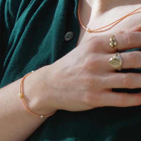 Zarte DIY-Halskette in Peach mit goldfarbenen Details und einer zentralen Süßwasserperle, getragen zu einem eleganten, dunkelgrünen Oberteil. Die minimalistische Kette aus dem Schmuckset von ever so tiny betont den filigranen und hochwertigen Stil.