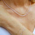 Nahaufnahme eines Dekolletés mit zwei zarten Halsketten. Die erste Kette besteht aus kleinen, lavendelfarbenen Glasperlen, die zweite ist eine feine goldene Gliederkette mit kleinen goldenen Perlen als Akzent. Dazu wird ein passendes Armband aus einer Kombination von lavendelfarbenen Glasperlen und einer goldenen Kette getragen. Der Look ist elegant und dezent, ideal für einen stilvollen und persönlichen Stil.