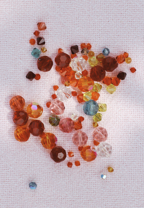 Verschiedenfarbige, geschliffene Glasperlen von Swarovski n Rot-, Orange-, Gelb- und Blautönen auf rosa Stoff. Hochwertige Perlen in unterschiedlichen Größen, perfekt für funkelnde DIY-Schmuckprojekte.