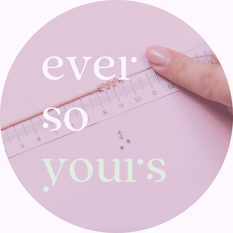 Ein kreisförmiges Bild mit dem Schriftzug „ever so yours“. Im Hintergrund misst eine Hand ein Armband mit einem Lineal auf einem rosa Untergrund ab. Kleine Perlen liegen daneben, was den DIY-Charakter und die individuelle Anpassung von Schmuckstücken bei "ever so tiny" betont. Das Bild symbolisiert die Personalisierung und die handwerkliche Präzision, die in jedes Schmuckstück einfließt.