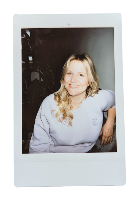 Ein Polaroid-Foto von Kathrin, einer der Gründerinnen von "ever so tiny". Sie trägt einen pastellfarbenen Pullover mit dem "ever so tiny" Logo und lächelt in die Kamera. Ihre blonde, wellige Frisur und das freundliche Lächeln strahlen eine entspannte und positive Atmosphäre aus. Das Bild vermittelt einen persönlichen Einblick in Kathrins Persönlichkeit und ihre Leidenschaft für das Projekt.