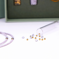 Close-Up auf DIY-Schmuckset von ever so tiny für eine Halskette in Lavendelfarben mit goldfarbenen Details und Swarovski-Kristallen. Präsentiert in einer hochwertigen, jadegrünen Box mit edler Goldprägung. Das Set enthält Glasperlen, Verschluss und eine Schritt-für-Schritt-Anleitung für die einfache Schmuckherstellung. Im Vordergrund ist ein fertiges Beispiel der Kette zu sehen.