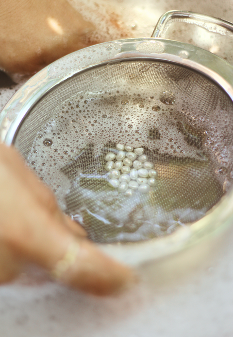 Reinigung von recycelten Süßwasserperlen in einem Sieb mit Seifenwasser, um ihnen neues Leben für nachhaltigen DIY-Schmuck von ever so tiny zu schenken.