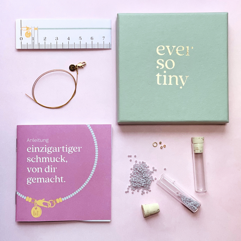 Ein DIY-Schmuckset von „ever so tiny“, bestehend aus einer mintfarbenen Schmuckbox mit goldener Prägung, goldfarbenem Schmuckdraht, einer lila Anleitung, Maßband, Glasperlen in einem Röhrchen mit Korkverschluss und kleinen Zubehörteilen.

DIY-Schmuckset von „ever so tiny“: Hochwertige Materialien wie Glasperlen, goldfarbener Schmuckdraht und nachhaltige Verpackung. Enthält Anleitung und Zubehör für einzigartigen, selbstgemachten Schmuck. Ideal für kreative Projekte und besondere Gesche